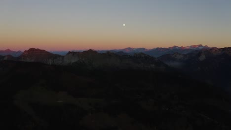 aerial shot of mountain range at sunset, pink summits and the moon rising the alps, switzerland