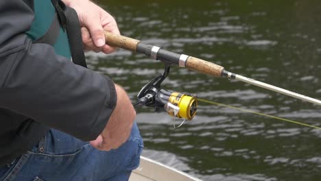 slow-motion close-up of fisherman’s hands reeling fishing line with water and jeans visible in background.
