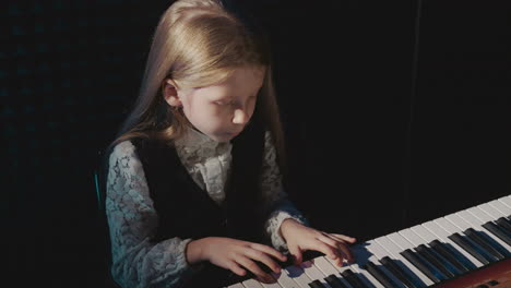 preschooler child performs tune on electric keyboard. fair-haired petite girl plays musical composition in recording studio. acoustic children performance