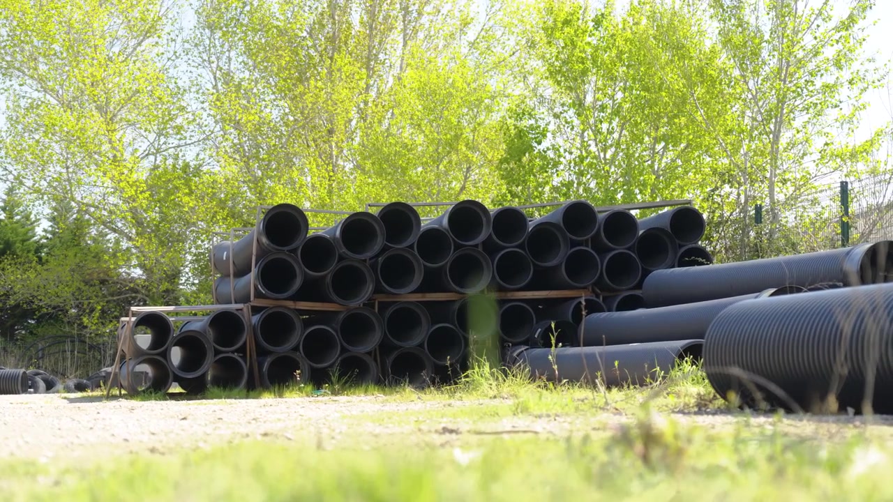 Large rigid pipes are stacked outdoors in an irrigation company's yard