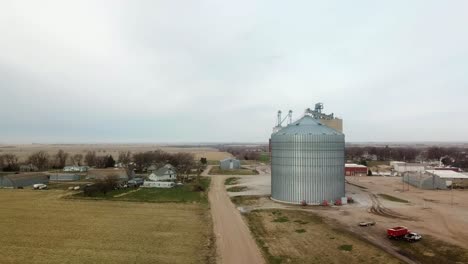 Vista-Aérea-Ascendente-De-Los-Contenedores-De-Almacenamiento-De-Granos-En-El-Borde-De-Una-Comunidad-Rural-En-El-Medio-Oeste