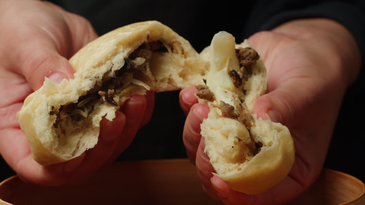 Hands Tearing Open a Steamed Bun with Meat and Cabbage Filling
