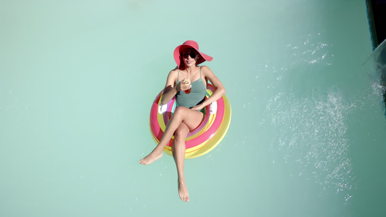 Relaxing on pool float, woman in swimsuit and sunhat enjoying drink