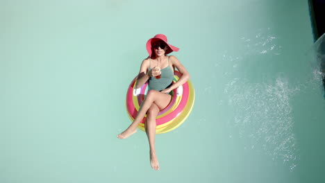 Relaxing on pool float, woman in swimsuit and sunhat enjoying drink