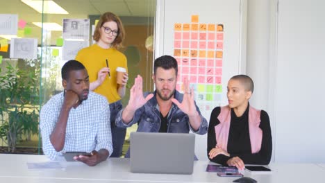 Mixed-race-business-team-discussing-over-laptop-in-modern-office-4k