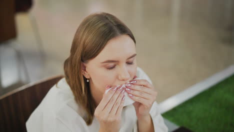 close-up of lady cleaning mouth with napkin while sitting alone at table in mall, soft blur background with chairs and tables in cozy mall dining area