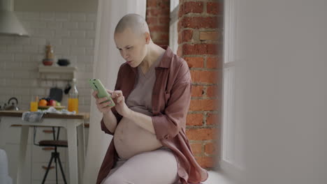 pregnant woman using a smartphone by the window