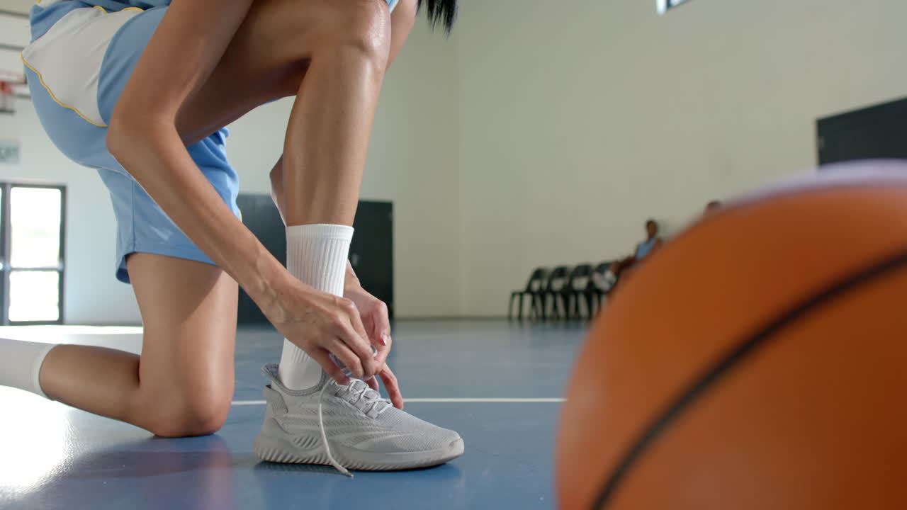 Tying shoelaces, female basketball player preparing for practice on court