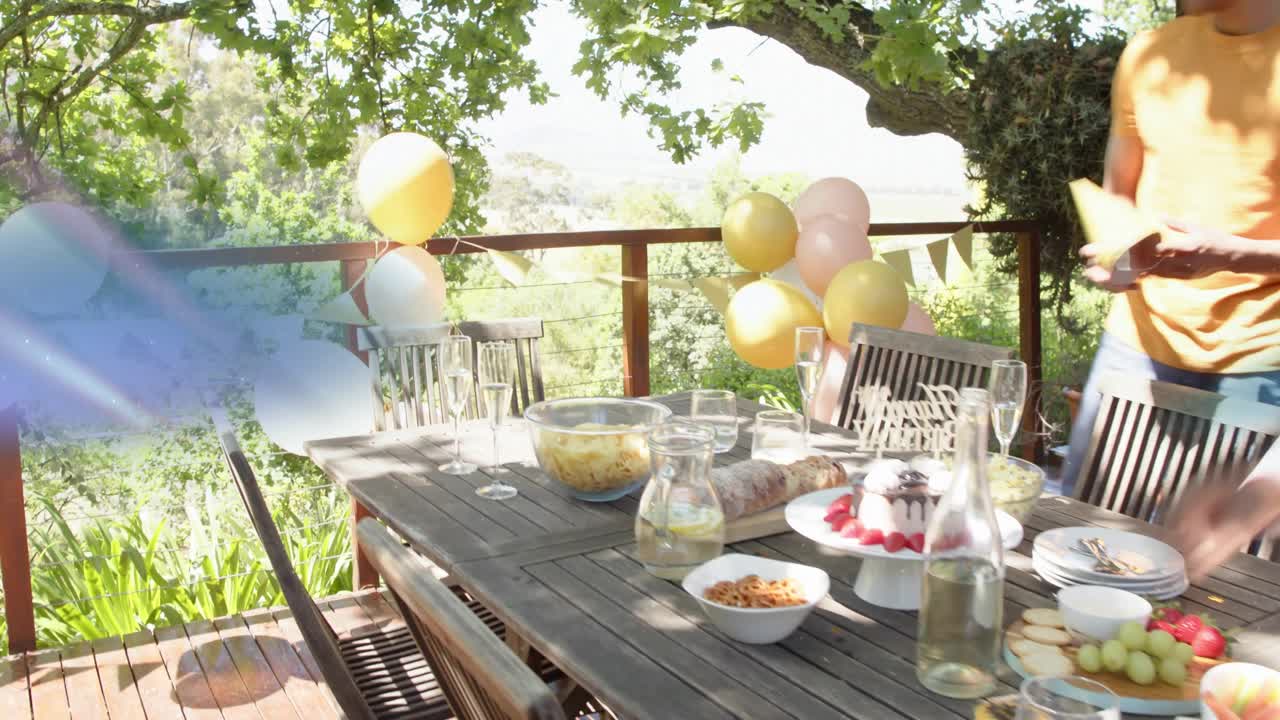 Hosts preparing table for event, woman fixing balloons, guest arriving with plates filling table