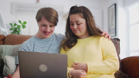 young downs syndrome couple sitting on sofa using laptop at home