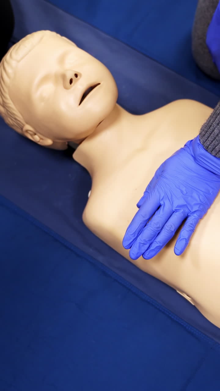 Training on a medical mannequin doll. Learning to do chest compression on a dummy. First aid cardiopulmonary resuscitation training. Top view. Vertical video