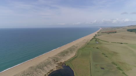 Aerial-tracking-forward-high-above-Chesil-Beach-at-Abbotsbury-looking-along-the-coastline-to-the-west