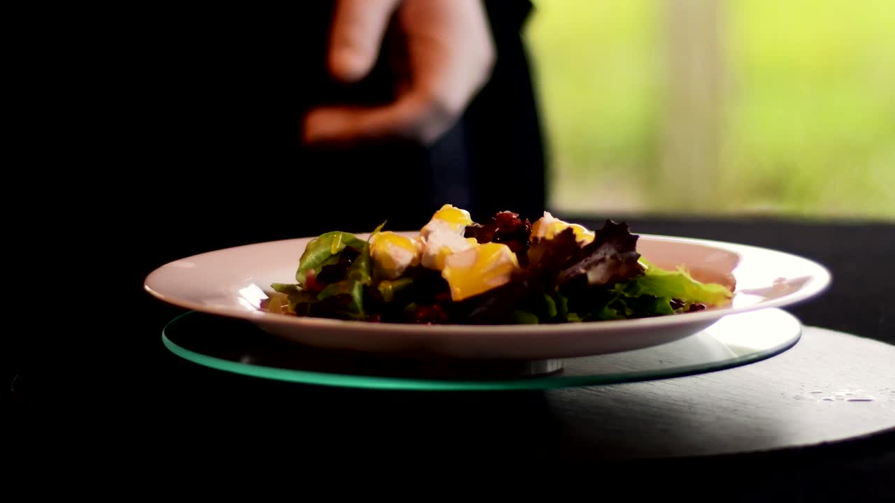 Ein Gericht mit Salat wird von der Hand eines Kochs gedreht und mit einer Serviette gereinigt