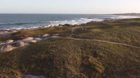 Persona-Irreconocible-Caminando-Sobre-Dunas-Con-Mar-De-Fondo,-Punta-Del-Diablo-En-Uruguay