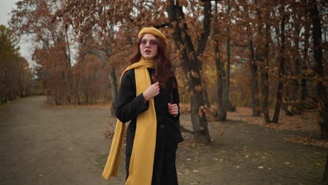 focused tourist in yellow muffler and beret walks through forest, adjusting hair and holding bag strap, deeply immersed in her journey