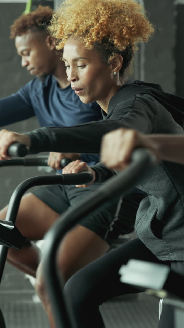 Determined Woman and Man Cycling on Stationary Bikes in a Gym