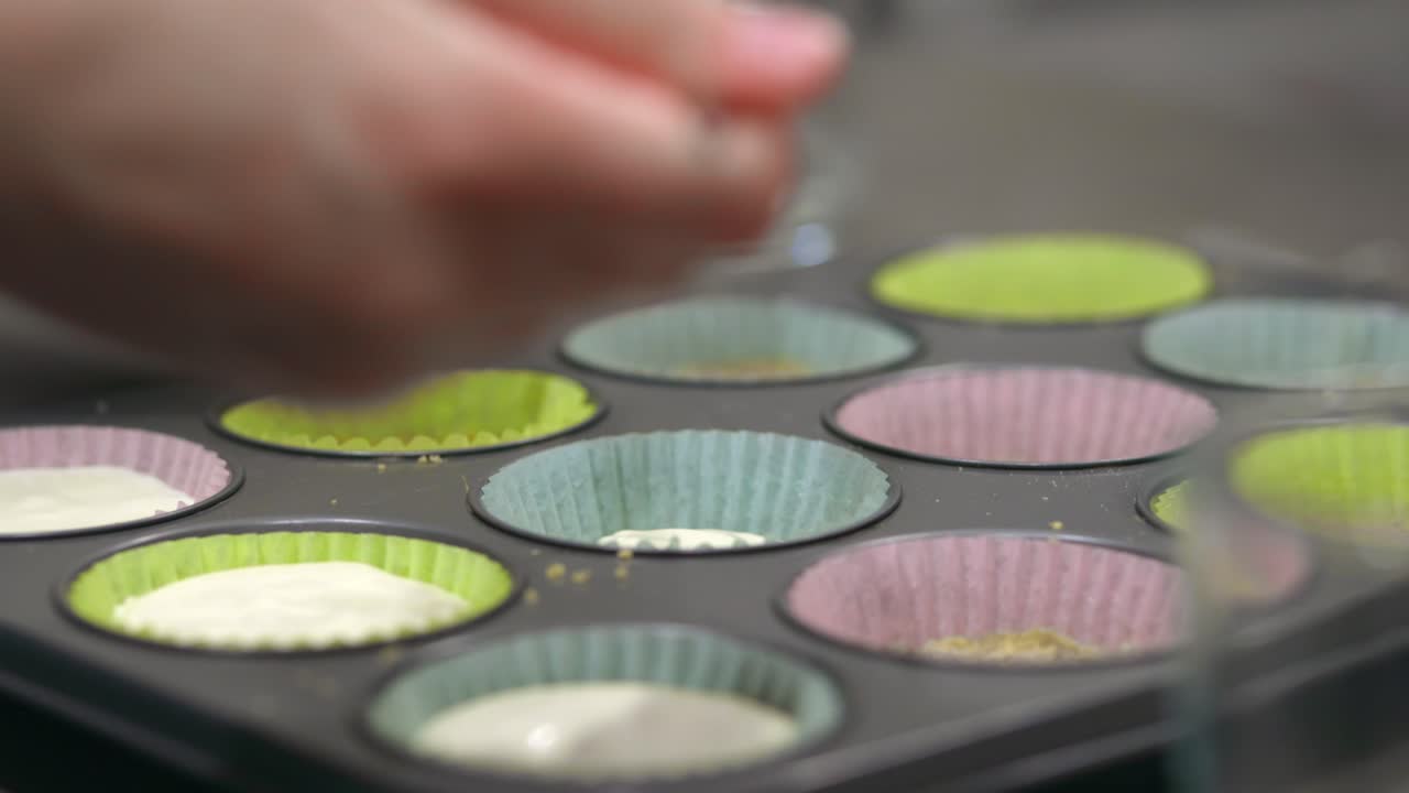 머핀 팬에 앉아 치즈 케이크 컵을 만들기 위해 미니 머핀 홀더를 채우기 위해 숟가락으로 채우는 치즈 케이크 크림을 퍼내는 여성