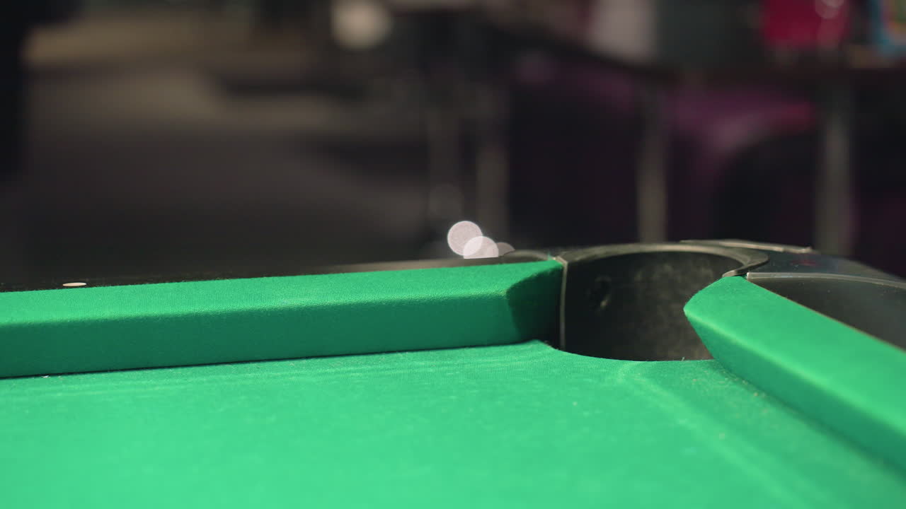 Sur un arrière-plan flouté, un gros plan capture une boule de billard rouge roulant rapidement dans la poche d’une table de billard sur une surface verte. Le flou de mouvement met en évidence la vitesse, la précision, la tension et l’excitation compétitive.