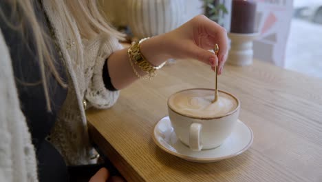 female slowly stirring cup of coffee with golden spoon in cafe