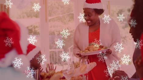 Animation-of-snow-falling-over-smiling-family-with-santa-hats-having-dinner