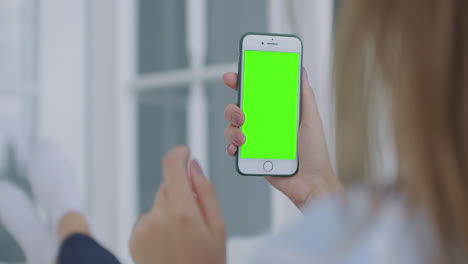 Woman-using-for-video-call-mobile-phone-vertical-green-screen.-Female-holding-in-hand-portable-gadget-close-up-indoors-home-living-room.-Mock-up-for-tracking-or-watching-content.