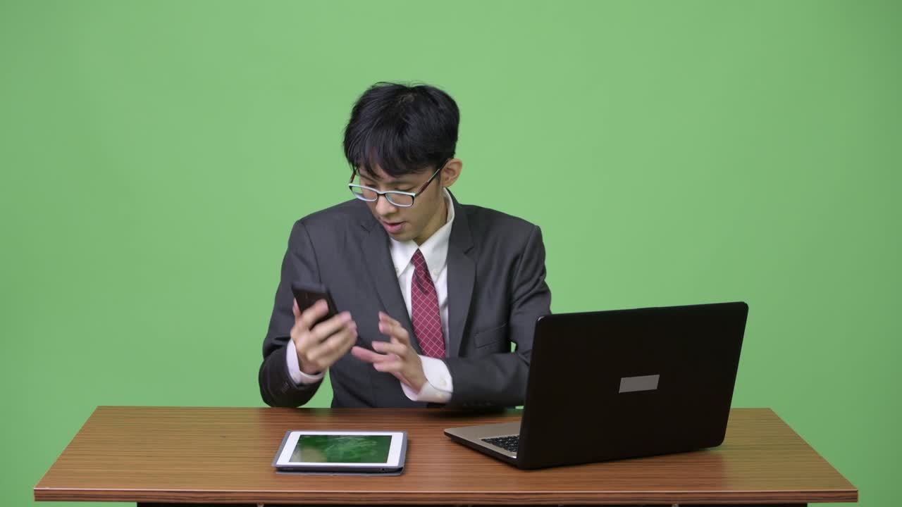 젊은 행복한 아시아 사업가가가 일하는 동안 전화로 비디오 통화를 합니다.
