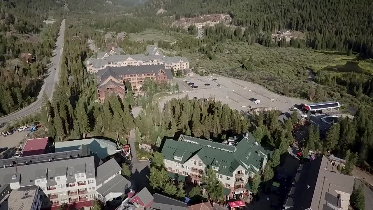 Drone shot looks down on a small village in Colorado and tilts up to reveal the surrounding mountains and blue sky.