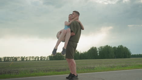 playful scene man lifting woman high beside country road as she jumps into arms then nearly drops her under moody sky capturing joyful moment of trust and laughter amid open landscape
