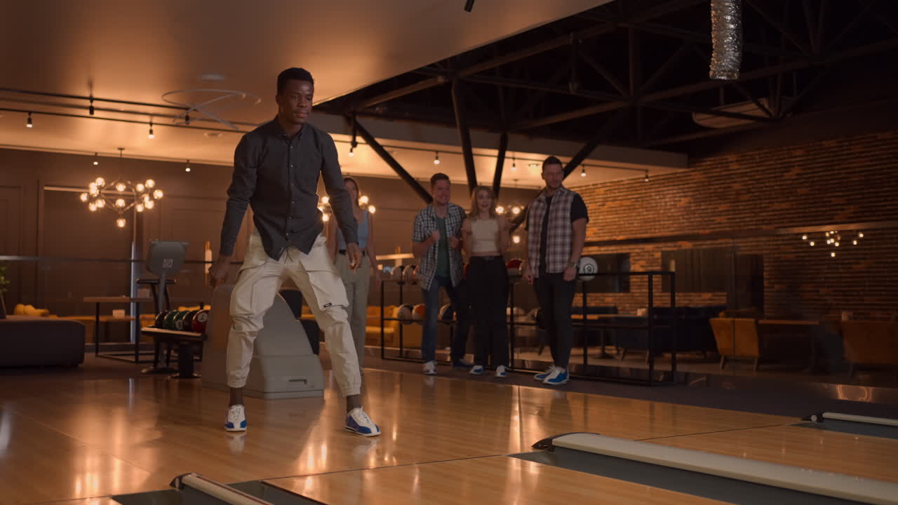 A black man makes a throw in a bowling club and enjoys emotionally knocking out pins with a ball