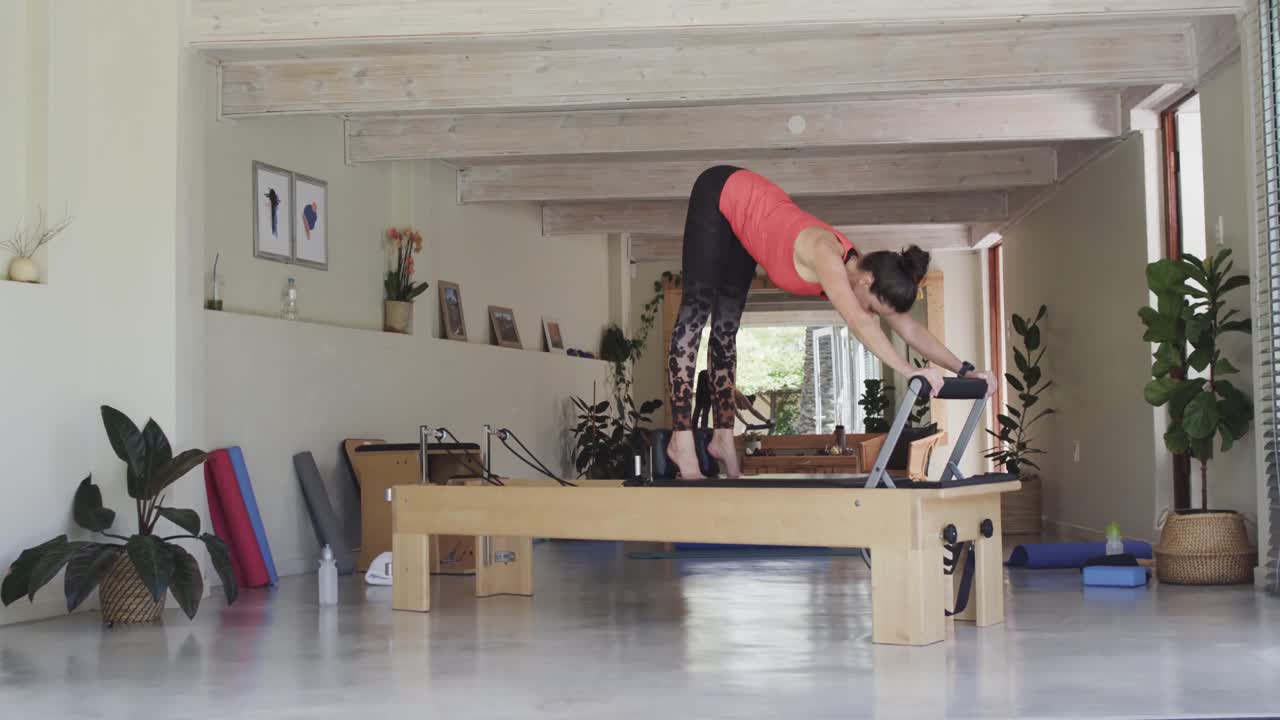 피트 시니어 백인 여성이 필라테스 스튜디오에서 리포머에 스트레칭하고, 변하지 않고, 슬로우 모션으로