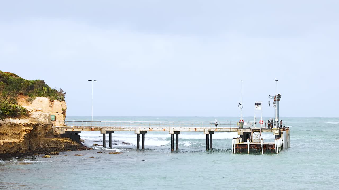 A serene pier extends into the ocean under soft daylight, surrounded by cliffs and calm waters
