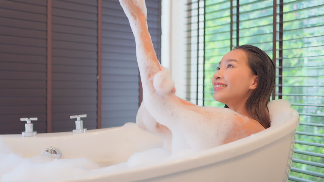 Close-up of a young healthy Asian woman taking a relaxing bubble bath while playing and washing with the bubbles