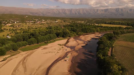 Gente-Relajándose-En-El-Río-Arenoso-Durante-La-Estación-Seca-Con-Montañas-De-Fondo-Al-Atardecer,-Córdoba-En-Argentina