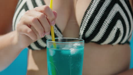 attractive woman in bikini shatters ice in a cocktail, close-up shot.