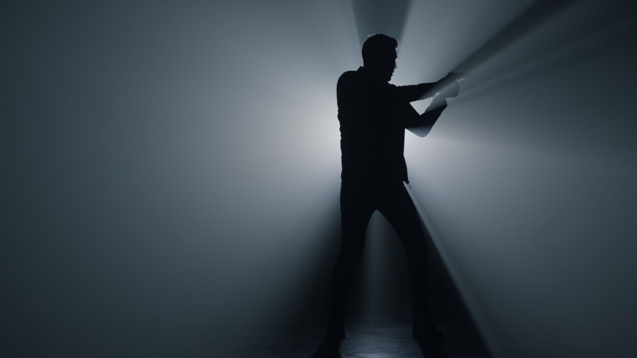 어 속에서 총을 겨냥하는 실루 남자. 총을 들고 주위를 둘러보는 총기.