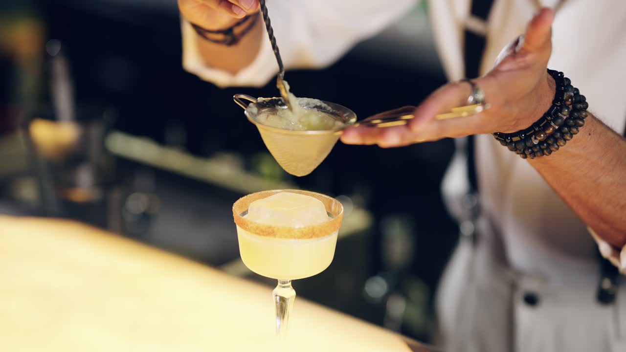 Barman che filtra un cocktail artigianale in un bicchiere al bancone del bar