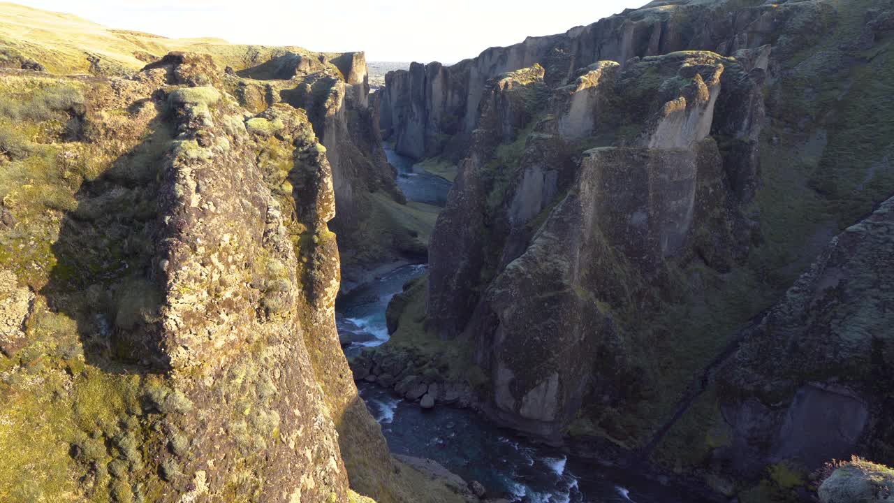 un majestuoso río que atraviesa un cañón verde en islandia, la luz del sol proyecta sombras, vista aérea