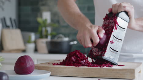 primer plano de un hombre rallando remolachas frescas con un rallador en una cocina moderna
