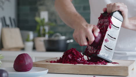 close-up of a man grating fresh beetroot with a grater in a modern kitchen