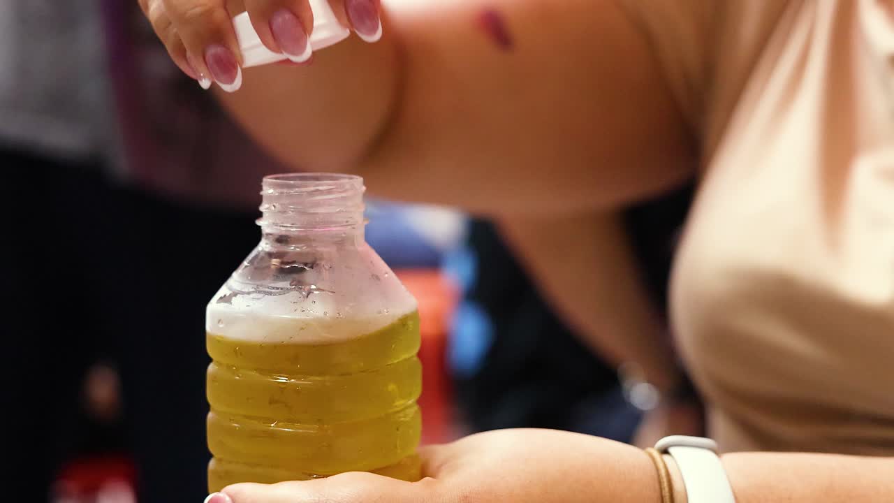 Close-up of woman unscrewing bottle cap, vibrant market background, natural lighting, handheld camera movement
