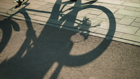 shadow of upside-down bike cast on ground as back tire rotates, activated by someone turning pedal, creating a dynamic silhouette effect under warm sunlight on pavement