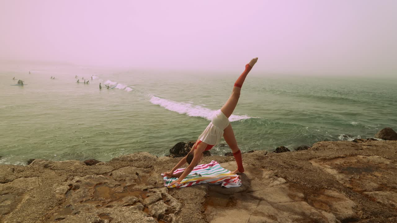 Donna che pratica yoga su una costa rocciosa con vista sull'oceano