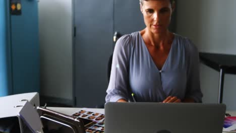 animación de una red de iconos digitales contra una mujer caucásica que usa una tableta gráfica en la oficina
