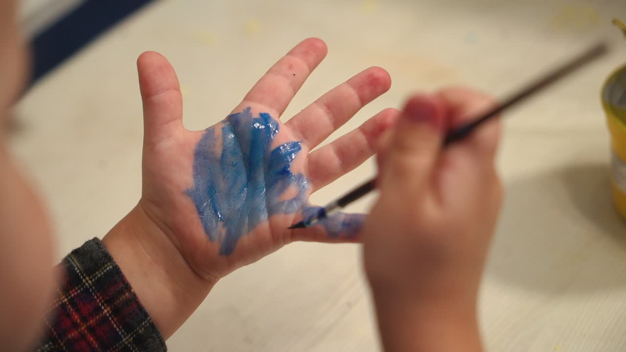 Funny child paints his hands with paint. Baby artist.