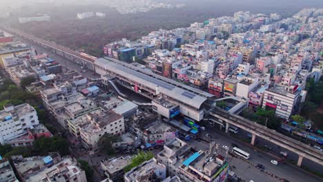 hyderabad metro train with station, buildings, and urban forest at day time, tilt down, stable shot, drone shot, 4k.