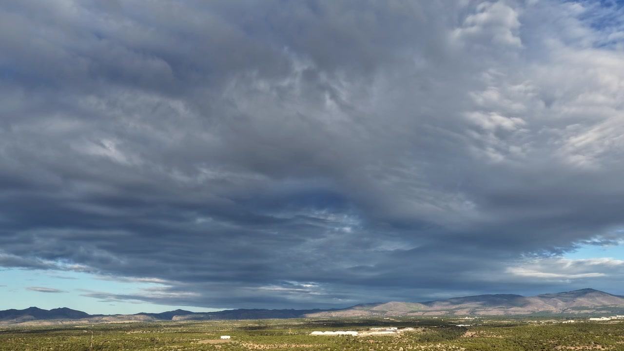 A cinematic 4K drone timelapse captures dramatic clouds sweeping across a vast landscape of southwest mesas. The rapid atmospheric motion over the desert vista creates an epic nature background.