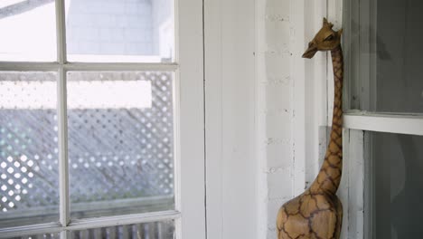 Handgefertigte-Giraffenstatue,-Die-Im-Wintergarten-Am-Fenster-Lehnt