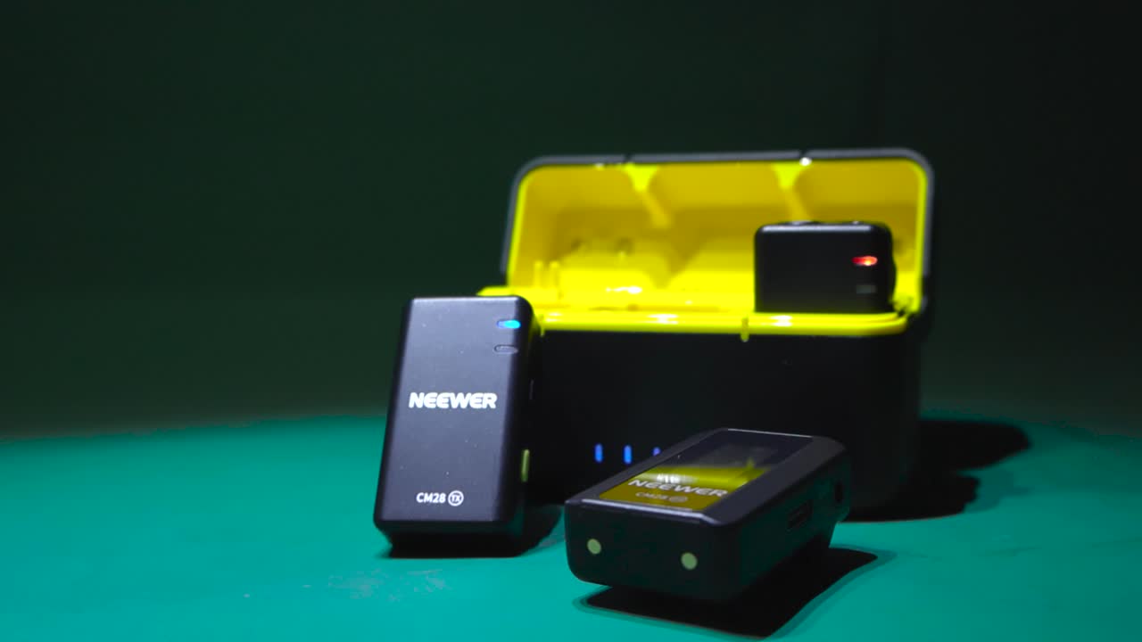 Cordless or wireless mic or microphone set kit placed on a green background. Neewer CM28 has a beautiful yellow storage box and lavalier microphones have audio jacks and led lights visible.