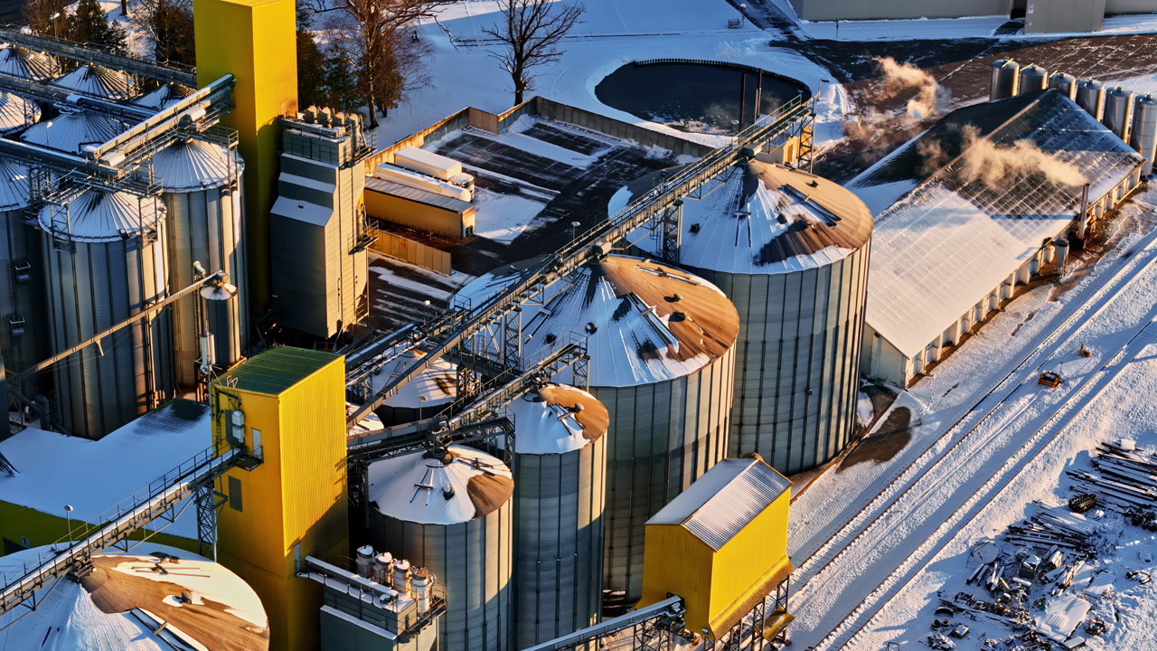 Aerial drone shot of an industrial grain silo complex with yellow buildings in winter snow
