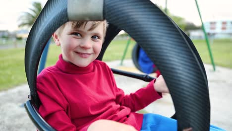 portrait of a cute boy making faces at the camera while on the swings at the playground